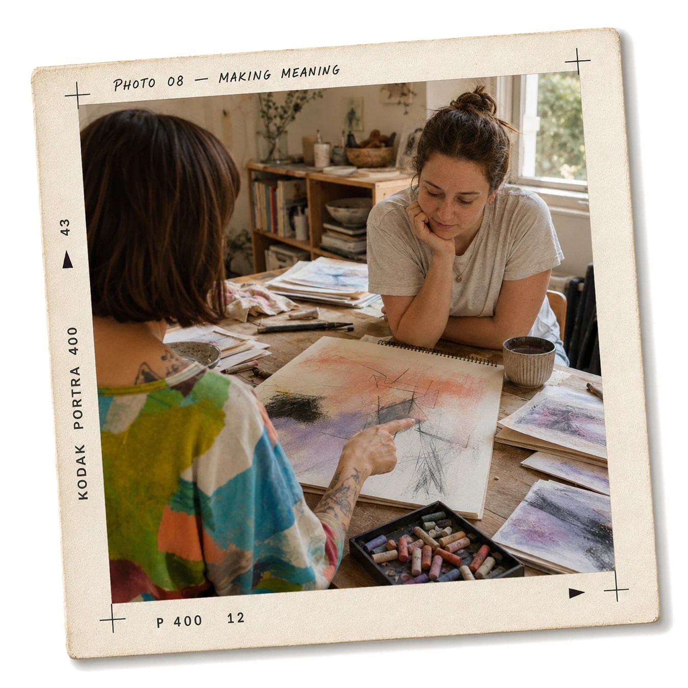 Jess sitting with someone at a table, discussing a pastel sketch together